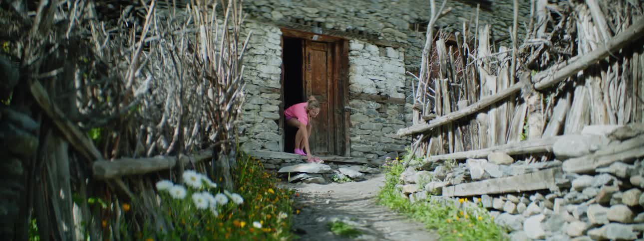 Woman walks out the door of a house in the countryside and puts her shoes outside