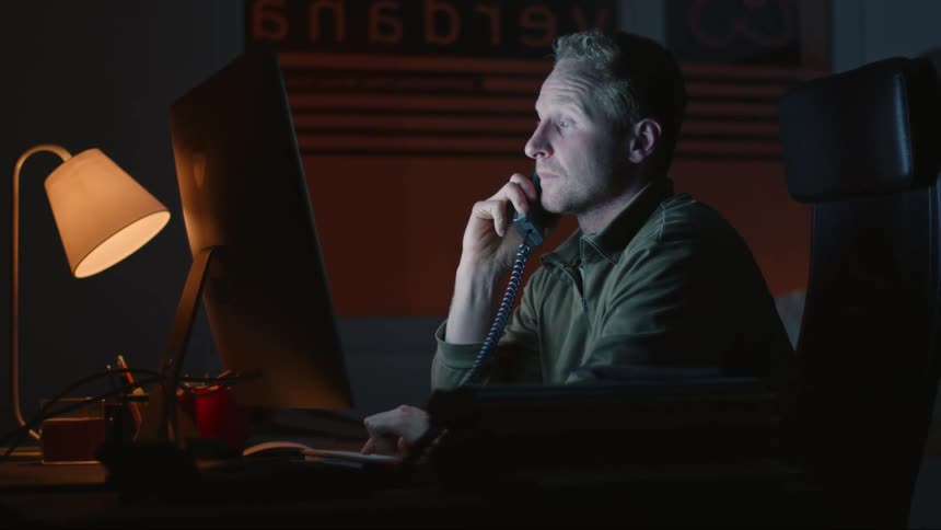 A man talks on the phone at his computer