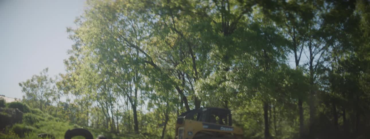 A small construction vehicle drives into the woods on a sunny day