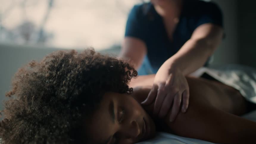 A professional masseuse uses her arms to rub the back of a woman laying on the table