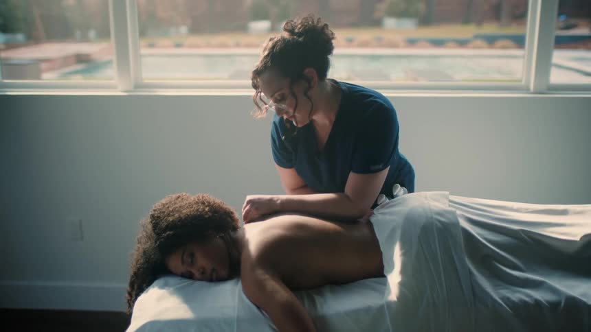 A professional masseuse uses her arms to rub the back of a woman laying on the table