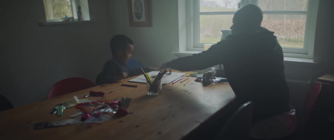 Father and son interact at dining table while child draws