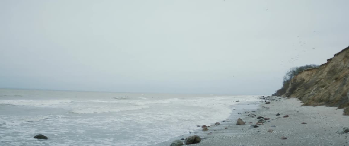 Gentle waves crash on the shoreline of a beach under an overcast sky at daytime