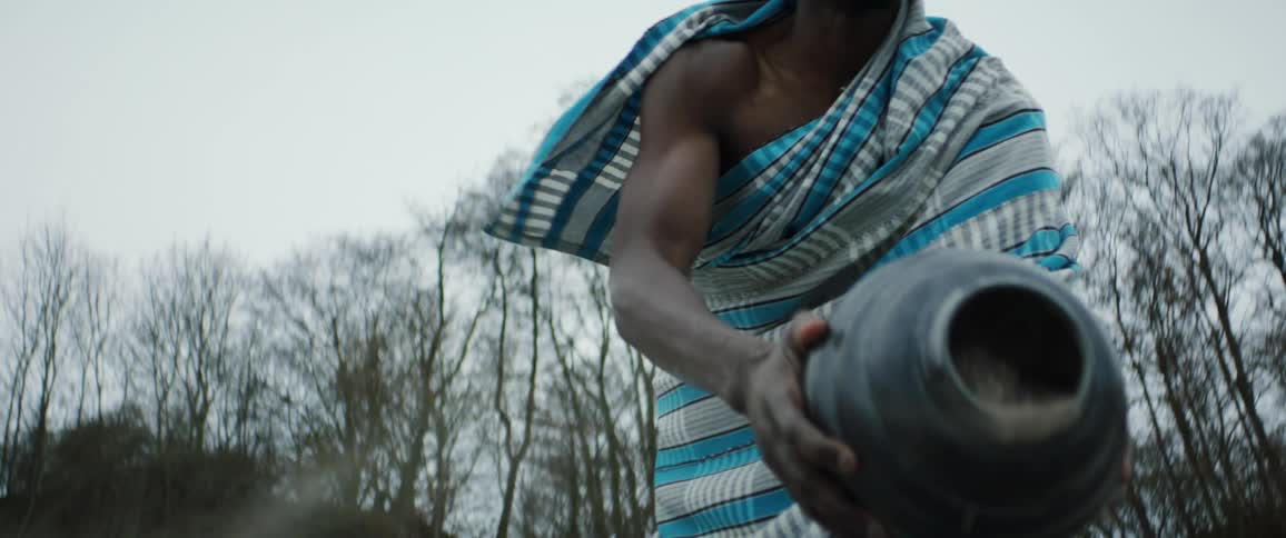 A man wearing a blue checkered cloth shaking dirt out of a black vase