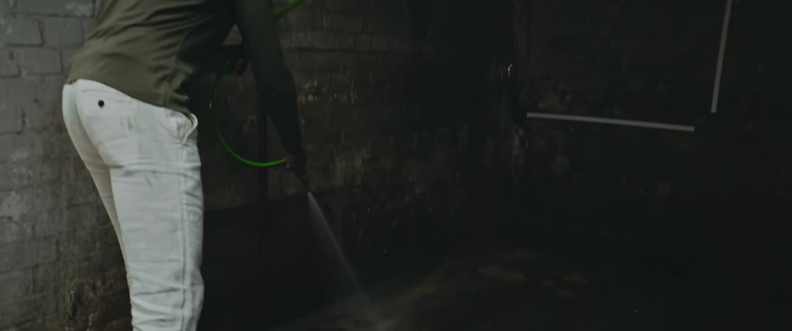 A man using a hose to spray out a concrete room