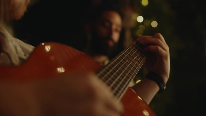 A man moves his hand across the neck of an acoustic guitar as he plays