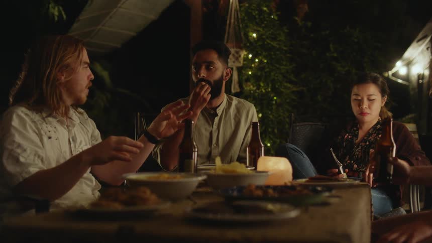 Group of friends talk while eating food at a party outdoors at night
