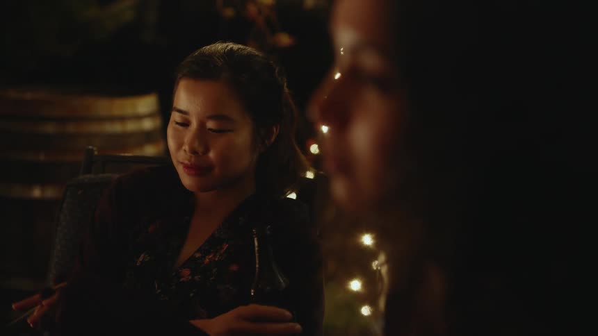 Two young women sit outside at night relaxing in silence with string lights behind them