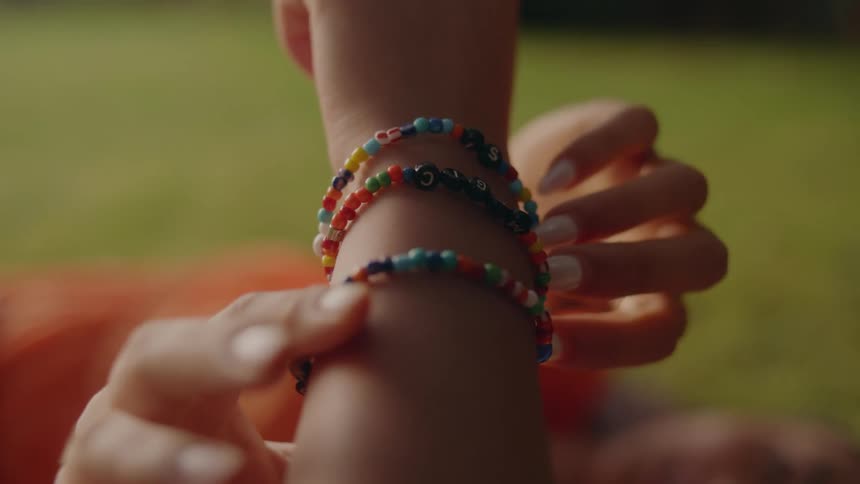 An up close of a persons wrist with bracelets on it as another hand twists the bracelet around