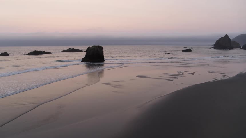 The glow of sunset reflects from the smooth sand of a beautiful beach dotted with sea stacks