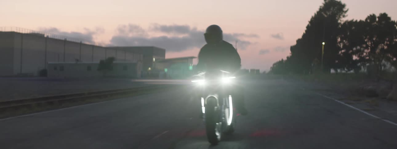 A person is driving a motorcycle on a road during dusk