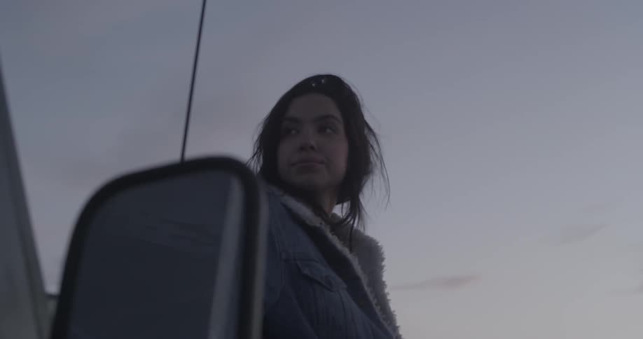 A woman stands outside at sunset