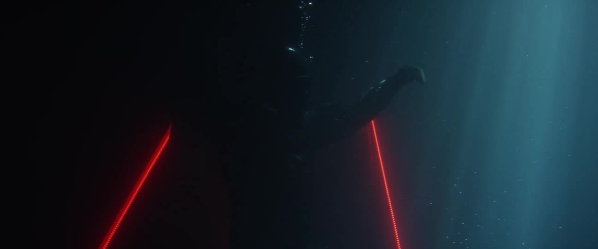 Person with motorcycle gear underwater with red neon lights and black background blowing bubbles