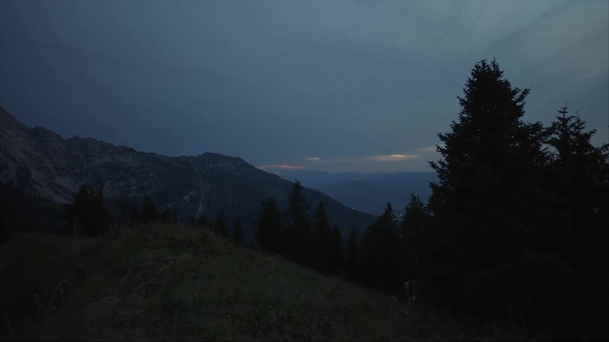 The sun sets through dense clouds over a mountain range