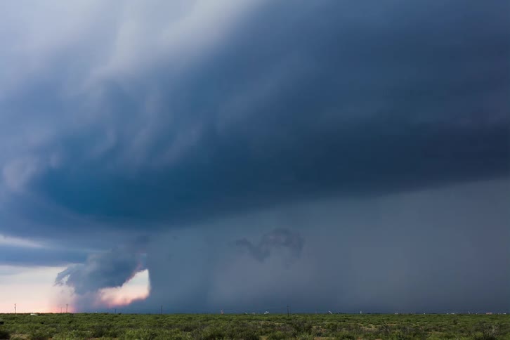 Dark storm clouds are moving and pouring rain over a rural area as lightning flashes