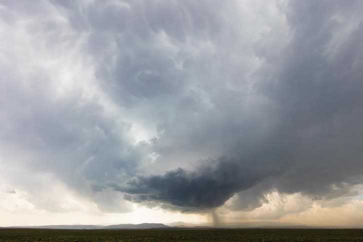Dark storm clouds move in rotation over a field as rain pours down from the clouds