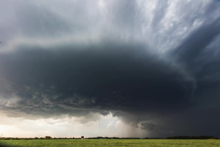 Dark storm clouds float in the sky over green field