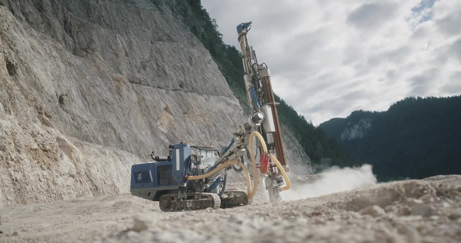 A construction truck is drilling a hole into the ground near a mountain cliff