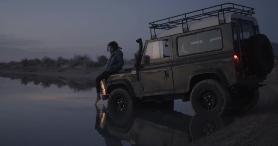 A woman sits on the hood of a car in the water