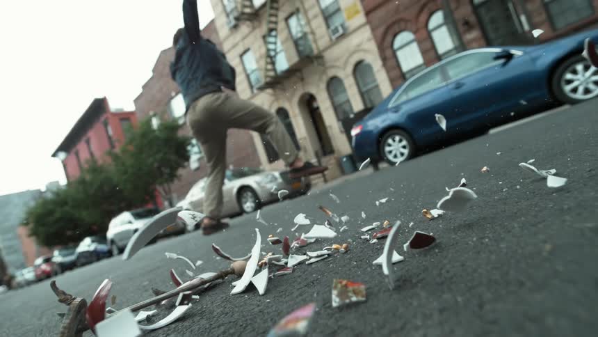 A man leaps backwards in the middle of a city street avoiding a vase crashing to the ground