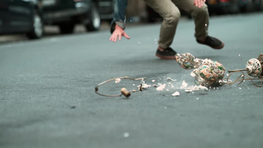 A man spins as an antique lamp falls and smashes on a city street