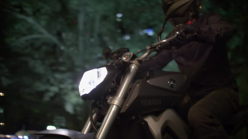 Headlights shine as a motorcycle travels on a city street at night