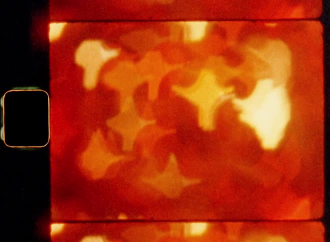 Old super 8mm film footage of a multitude of bright colorful lights that are very blurry creating a textured pattern of rectangular and star shaped bokehs with shaky downward camera movement