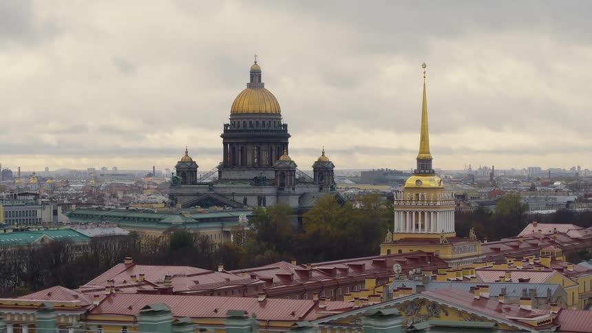 An aerial of the top of buildings with gold colored roofs surrounded by city buildings and streets