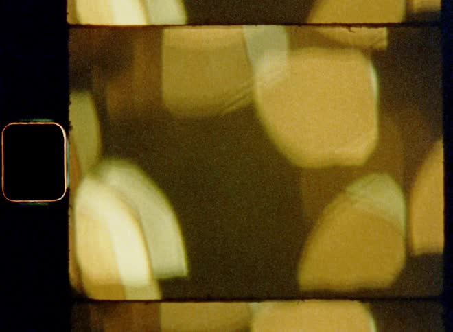 Passing city lights blur due to high-speed drive by out of focus creating rolling past motion of myriad of warm golden bokehs providing contrast and abstract light patterns on vintage Super 8 mm film with dynamic movement