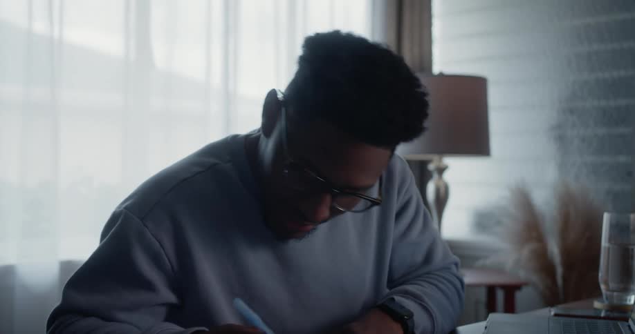 Man sits at desk working on laptop and writing things down