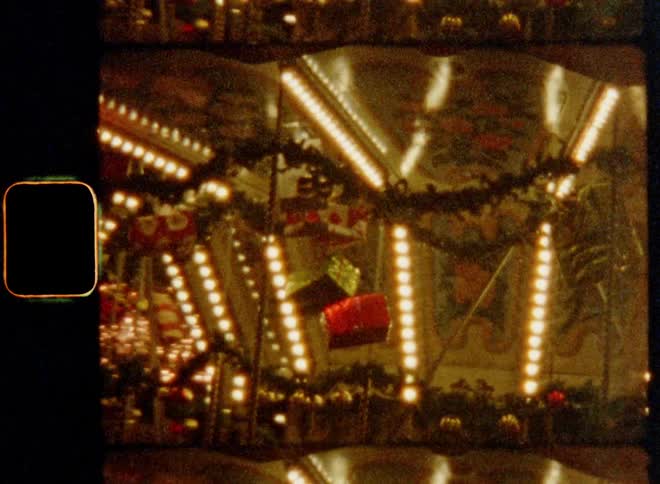 Merry go round carrousel with bright electric light bulbs of chains of lights and Christmas present décor turns fast as children enjoy the amusement ride in the good old days on a Christmas fair with holiday spirit and happy vibes on nostalgic 8mm film