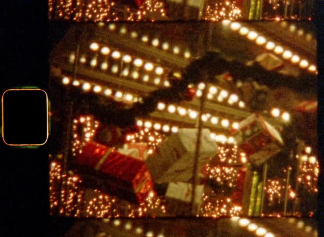 A spinning or rotating merry go round is decorated with light chains and wrapped packages or presents and multicolor decor with thousands of warm glowing lights of a leisure park or city scape in the background symbolizing the Christmas holiday spirit