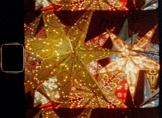 Handheld panning 8mm film footage of glowing Christmas stars and holiday decorations shine in a X-mas display at night as symbol for the Star of Bethlehem with bright colors creating a heart-warming and cosy advent atmosphere