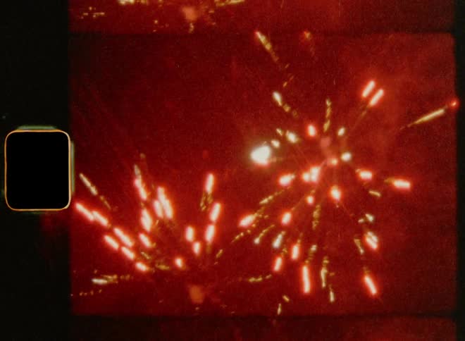 Several red fireworks explode in the dark night sky in front of the moon on July 4th on Super 8mm film