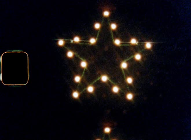 Bright lights of Christmas star made of electrical light bulbs from a chain of lights cause lens flare and abstract reflections against the black night sky as dark background on nostalgic vintage Super-8 film with upward tilting movement of the old camera