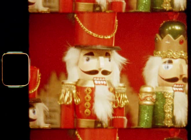 Multiple smiling nutcracker figurines and other handmade and crafted X-mas manikins are lined up next to each other on the table of a Christmas market stall booth or decoration or décor shop or store on nostalgic 8mm film