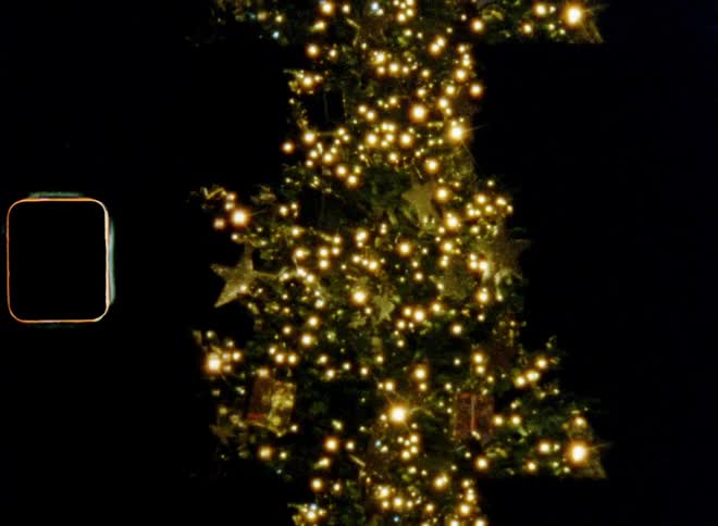 Blinking lights and warm golden candles shine and illuminate decorated Christmas tree with ornaments standing on the streets or town square during a market or fair for festive holiday atmosphere in advent on vintage film with retro vibes