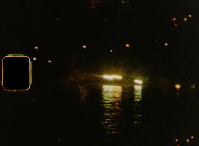 Colourful fireworks are shooting across a river with bright reflections on the surface of the water on old 8mm film