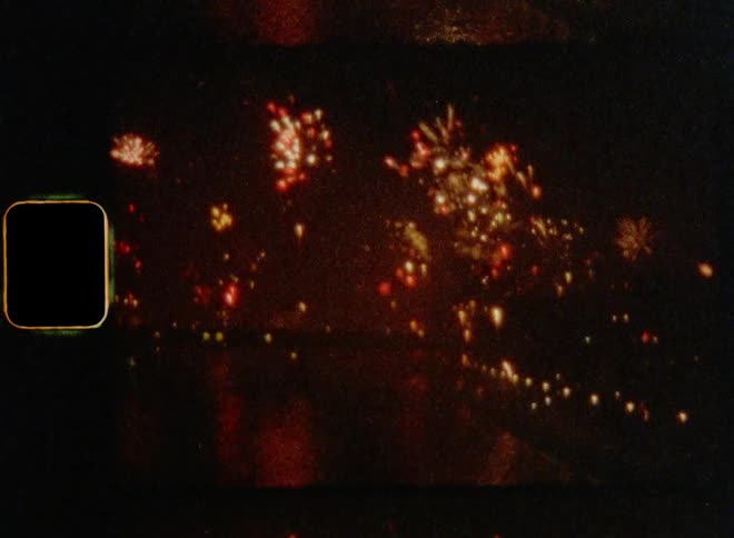 A flurry of sky rockets are fired off during a fireworks show held near the shoreline at night on 8mm with vintage film burn