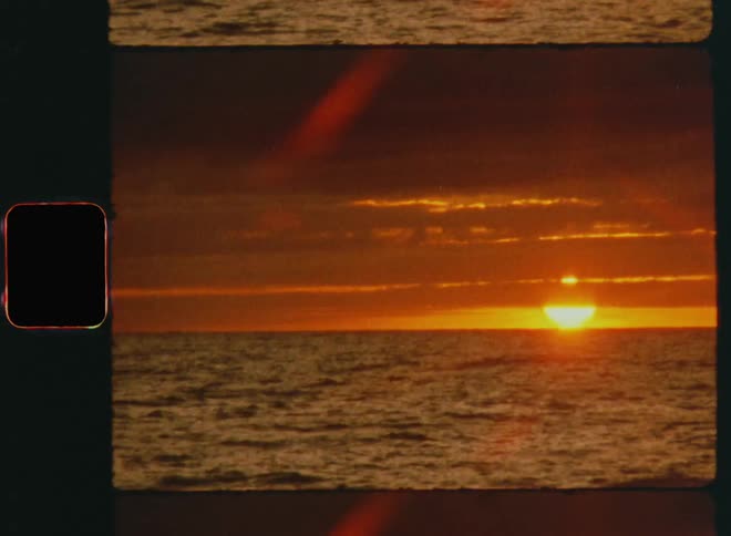 Time lapse view of the sun setting above ocean water with orange and red sky and glowing clouds while the waves move and the sunlight disappears at the horizon