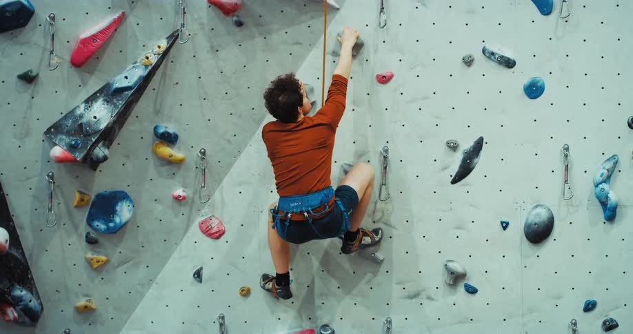 A man slips while climbing a rock wall and hits himself in frustration