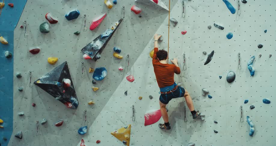 A man has a harness and rope around his waist and slips scaling a wall as he swings and from his rope