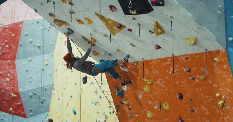 A man briefly hangs upside down while climbing in indoor rock wall