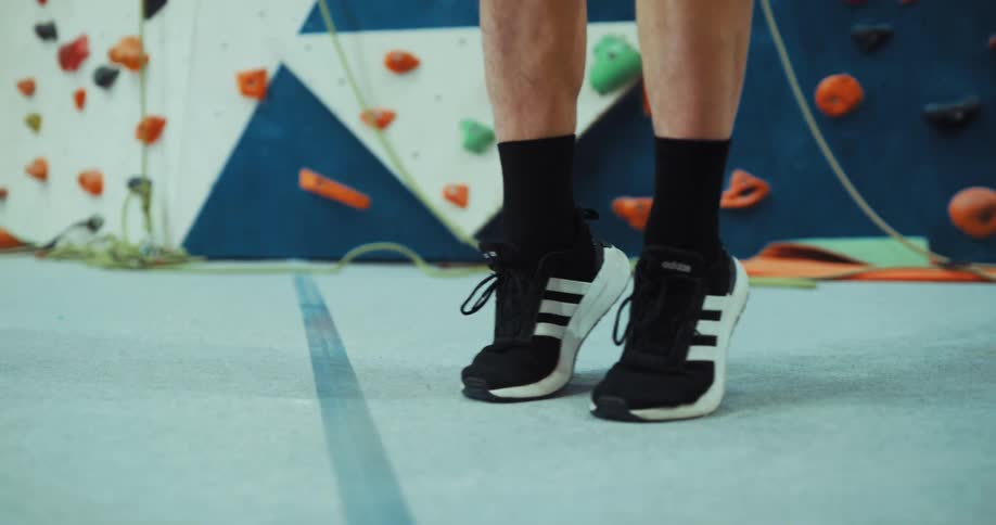 A man stretches his ankles and feet while standing in front of a rock wall