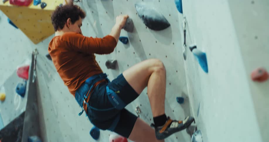 Man with orange shirt and blue shorts climbs a climbing wall