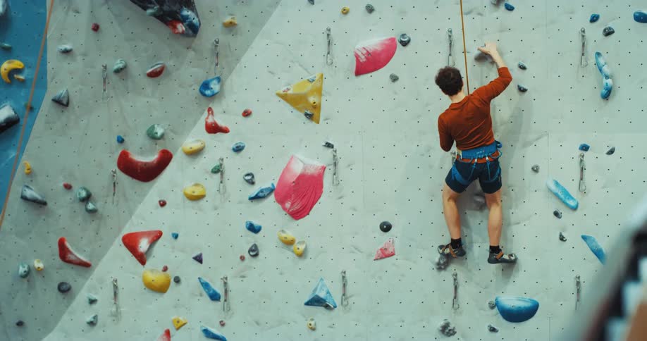 A man is climbing a rock wall while wearing a harness