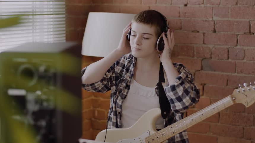 A woman holding a guitar puts on headphones