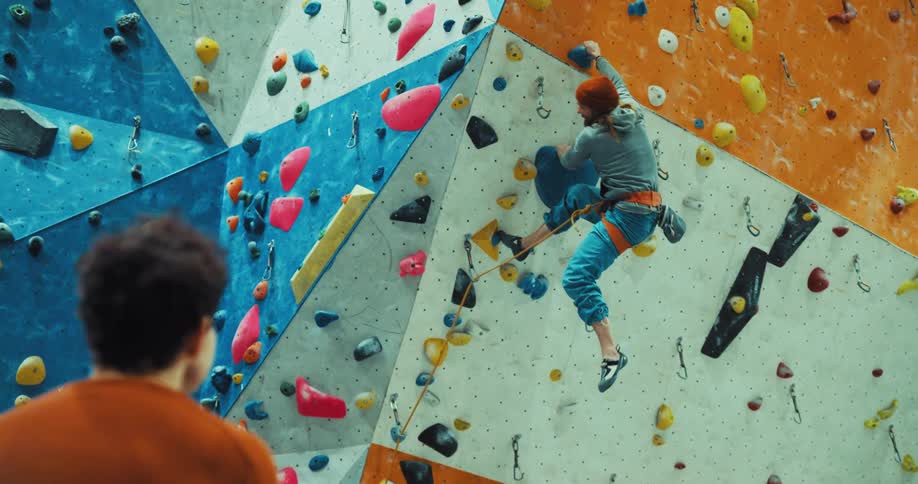 Man watches man climbing a climbing wall