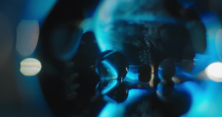 Blue light shines on clear spheres as a large blue and green round object moves in the distance
