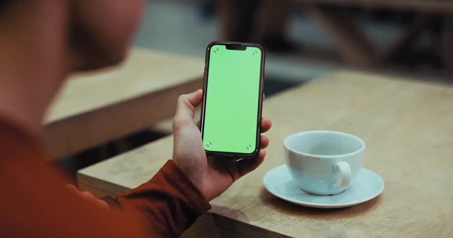 A man scrolls through his phone while sitting in a cafe